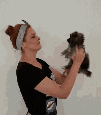 a woman in a black shirt holds a small dog in her hands