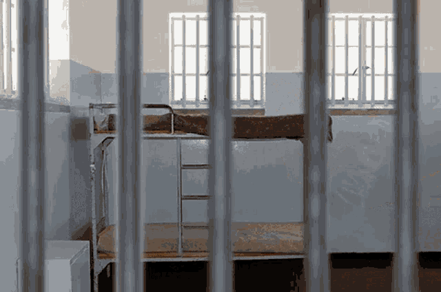 a prison cell with bunk beds and a window behind bars