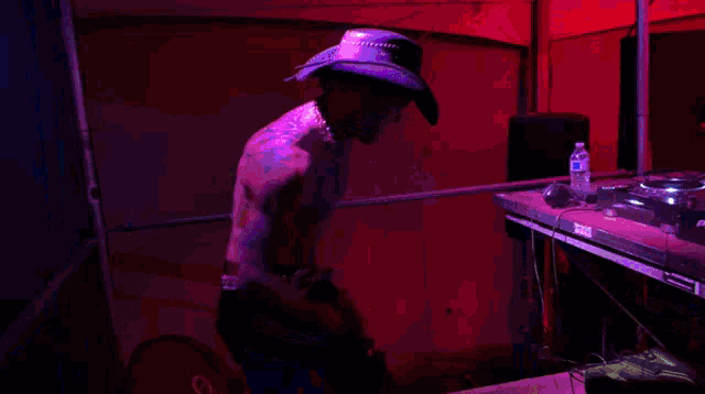 a shirtless man in a cowboy hat is standing in front of a dj booth