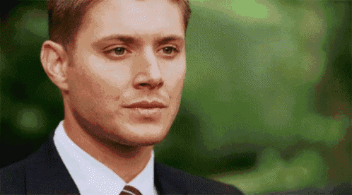 a man in a suit and tie is looking at the camera with a green background .