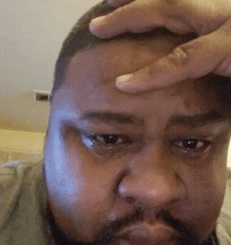 a man with a beard is holding his hand to his forehead and making a funny face .