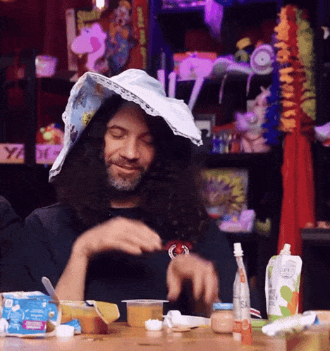 a man wearing a diaper on his head sits at a table with food