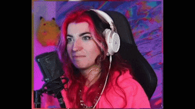a woman with red hair is sitting in front of a microphone wearing headphones and a pink hoodie .