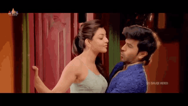 a man and a woman are kissing in front of a red door . the man is wearing a blue robe .