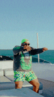 a man wearing green shorts and a green hat stands on a boat near the ocean