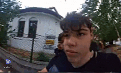 a young boy is standing in front of a white house with a fence behind him .