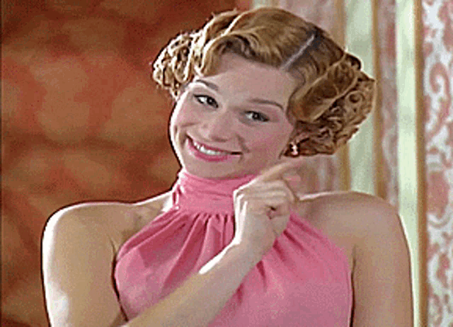 a woman in a pink dress is smiling and pointing at herself