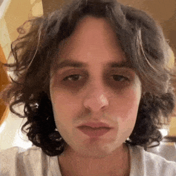 a close up of a man 's face with curly hair and a white shirt .