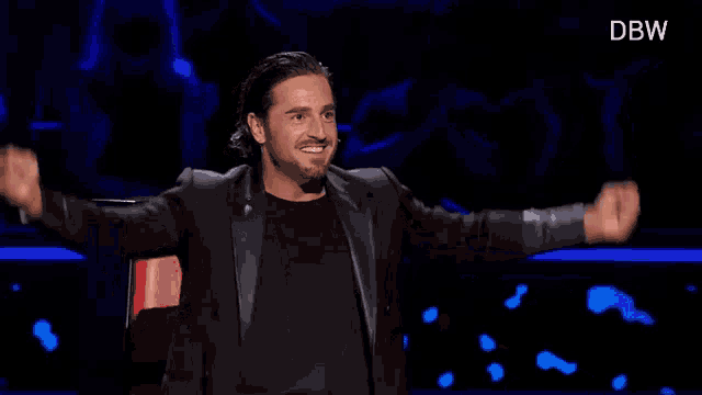 a man in a black suit is sitting in a red chair with his arms outstretched