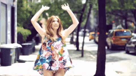 a woman in a floral dress is standing on a street with her arms in the air