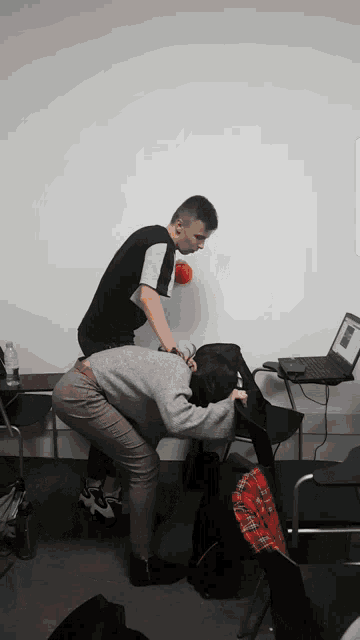 a man and a woman squatting down with a laptop on a desk