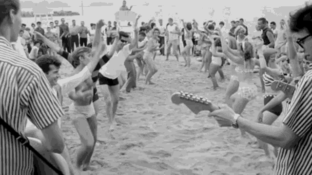 a man playing a guitar in front of a crowd of people dancing on the beach