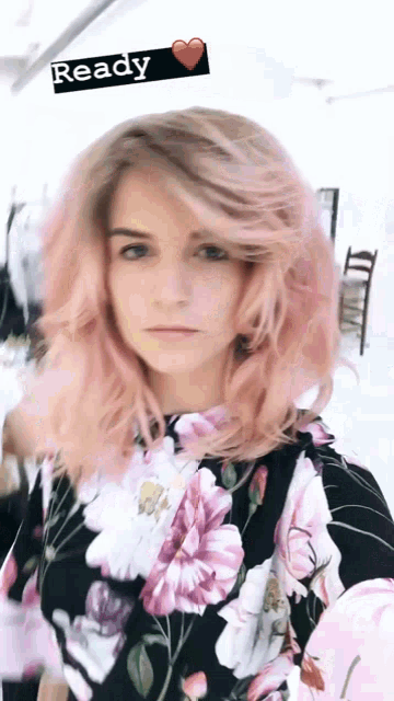 a woman with pink hair is wearing a floral shirt and has a ready sign above her head