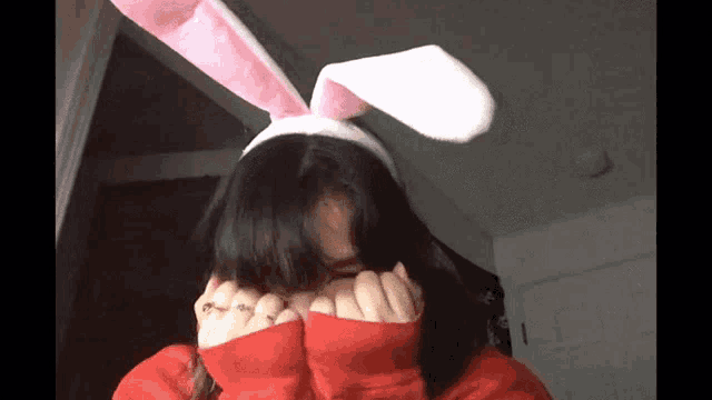 a girl wearing pink and white bunny ears covering her face .