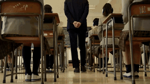 a man in a suit stands in front of a classroom filled with students