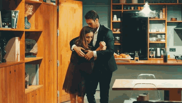 a man in a suit and a woman in a dress are hugging in a kitchen