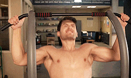 a shirtless man is doing pull ups on a machine in a gym