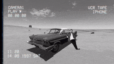 a black and white photo of a man standing next to a car that says camera 1 play