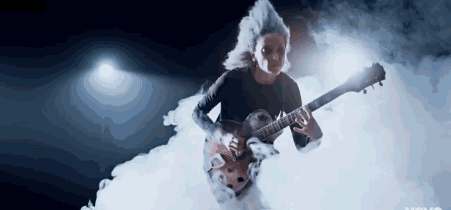 a woman in a black shirt is playing a guitar in a cloud of smoke .
