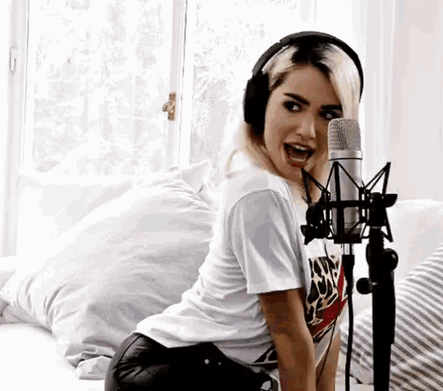 a woman wearing headphones is singing into a microphone while kneeling on a bed .
