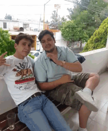 two men are sitting on a balcony with one wearing a california shirt