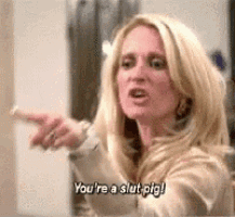 a blonde woman is pointing at something and saying you 're a slut pig .