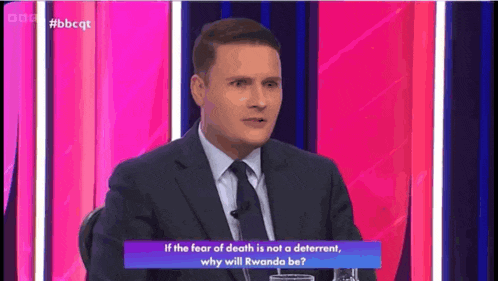 a man in a suit and tie is sitting in front of a pink and blue background while talking about death