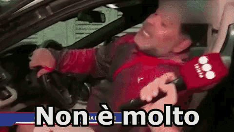 a man is sitting in a car with a microphone in his hand and says non e molto .