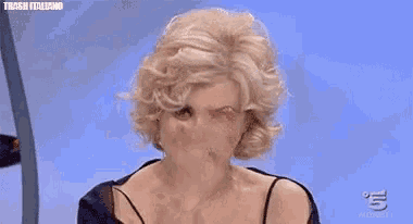 a woman with blonde hair is sitting in front of a blue background with the word amen on her chest .