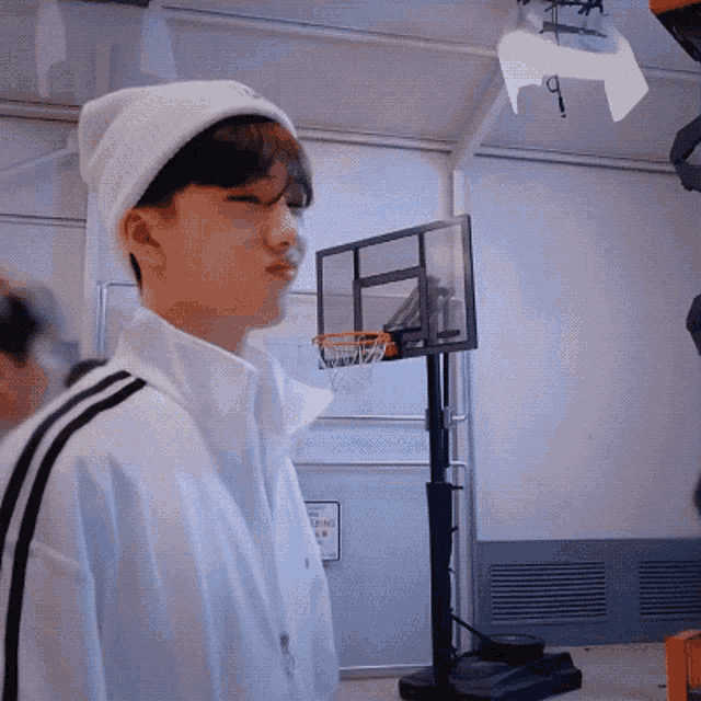 a young man wearing a white beanie is standing in front of a basketball hoop