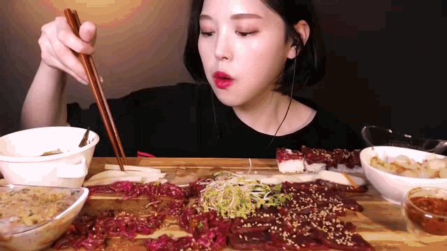 a woman is eating meat with chopsticks while wearing ear buds