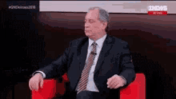 a man in a suit and tie is sitting in a red chair on a news channel .