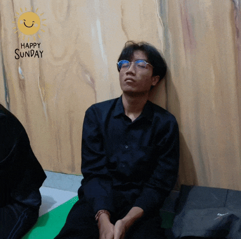 a man wearing glasses sits in front of a happy sunday sign
