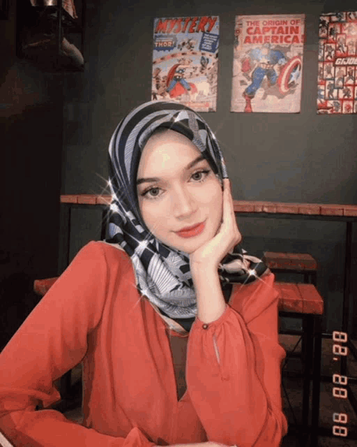 a woman wearing a hijab is sitting in front of a captain america comic book