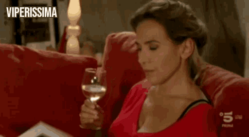 a woman is sitting on a couch drinking a glass of wine .