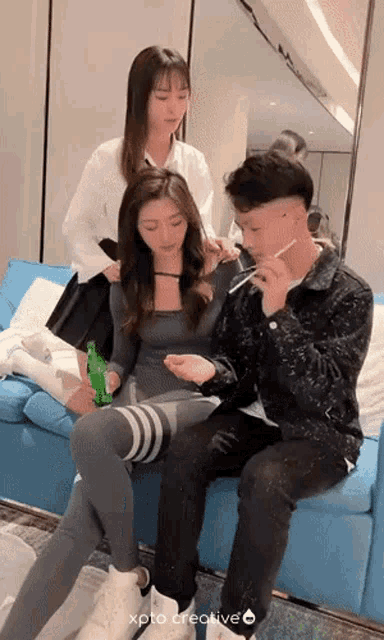 a man and two women are sitting on a blue couch and one of the women is holding a green bottle