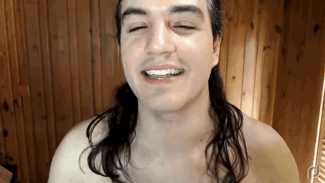 a shirtless man with long hair is smiling and looking at the camera