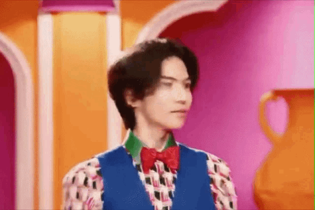 a man wearing a blue vest and a red bow tie is standing in front of a colorful wall .