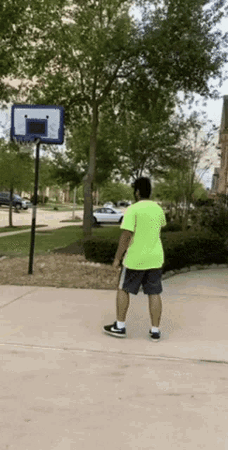 a man in a neon green shirt is playing basketball on a sidewalk
