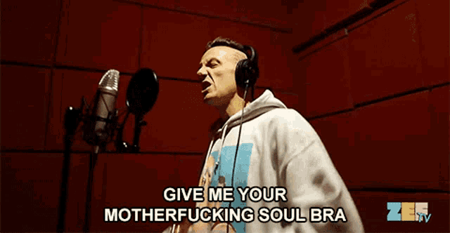 a man wearing headphones is singing into a microphone with the words give me your motherfucking soul bra above him