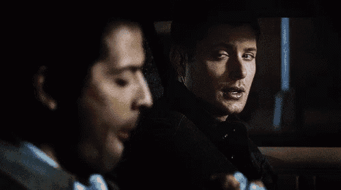 two men are sitting in the back seat of a car talking to each other .