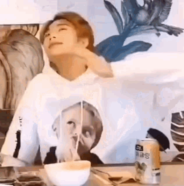 a person is sitting at a table with a bowl of noodles and a can of soda .