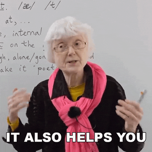 an elderly woman wearing glasses and a pink scarf stands in front of a white board that says " it also helps you "