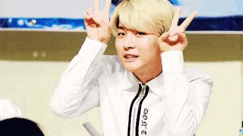 a young man in a white shirt is making a peace sign with his hands