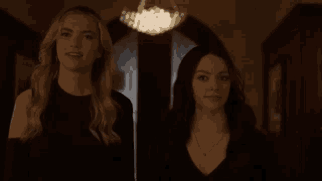two women are standing next to each other in a hallway looking at something .