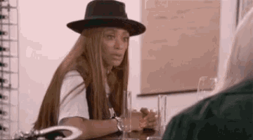 a woman wearing a hat is sitting at a table with a glass in her hand .