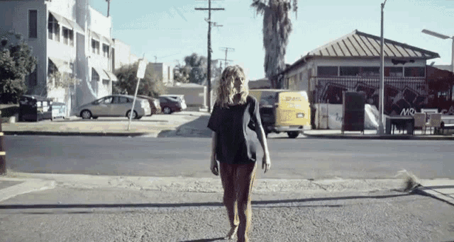 a woman crossing a street with a yellow van that says dhl on the back
