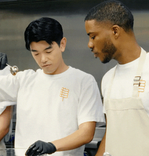 a man wearing a white shirt with the letter m on it is standing next to another man