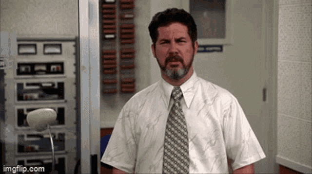 a man with a beard wearing a white shirt and tie is standing in a hallway ..