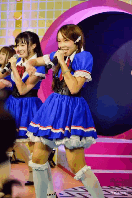 a girl in a blue dress sings into a microphone in front of a pink circle